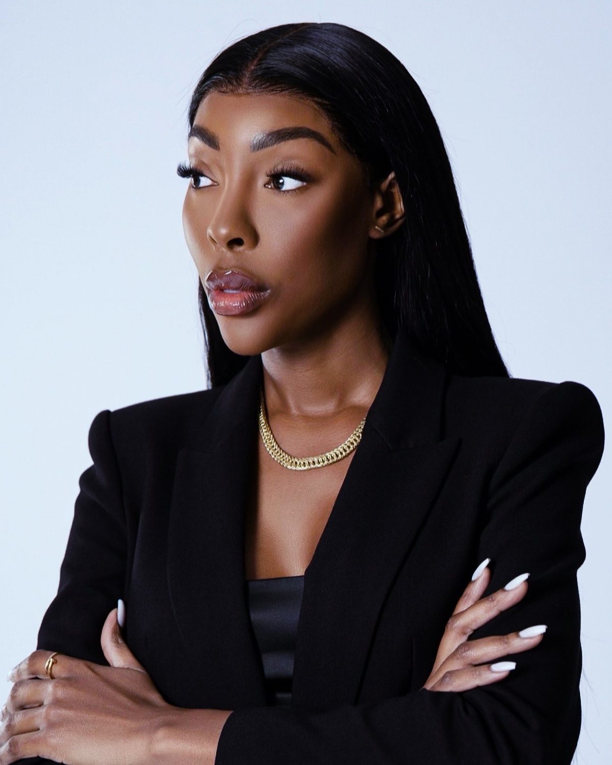 Woman in a black blazer with arms folded against a plain backdrop, studio headshot