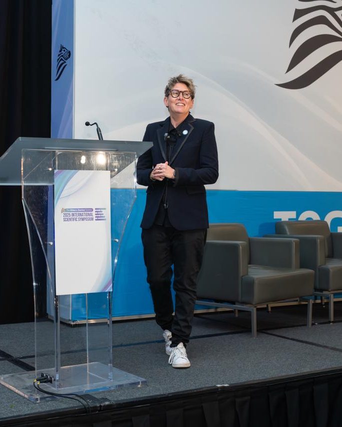 Speaker on stage in front of an Ehlers-Danlos Society backdrop at a medical conference