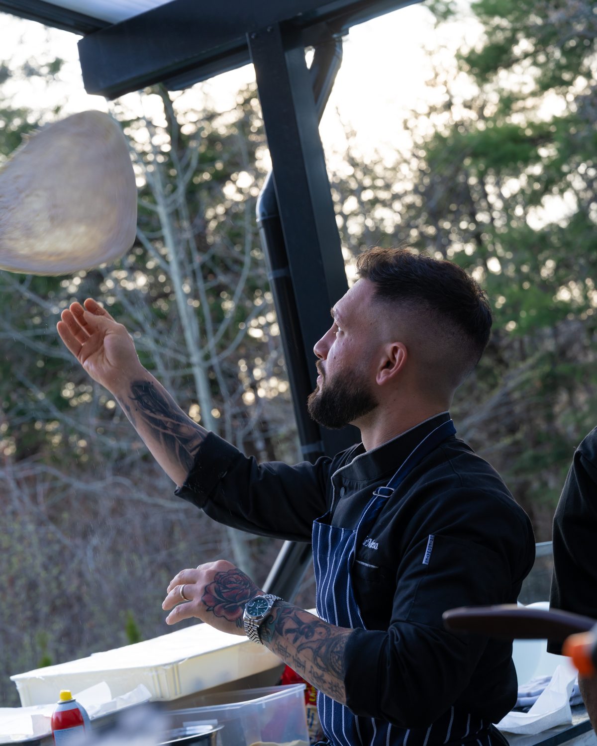 Chef in a striped apron tossing dough outdoors, lifestyle content photograph