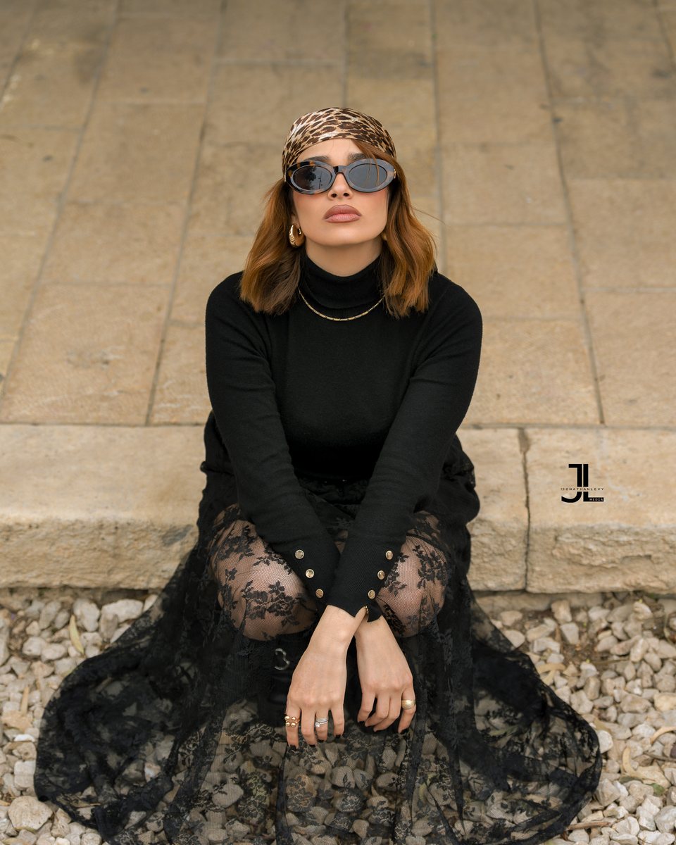 Woman in a black lace gown and embellished headpiece seated on gravel, editorial portrait