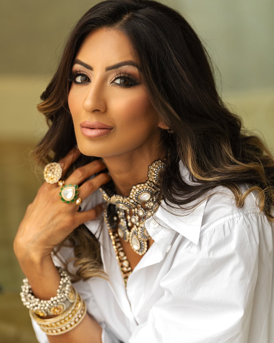 Woman in a white blouse and layered gold jewelry with her hand at her neck, luxury jewelry editorial portrait