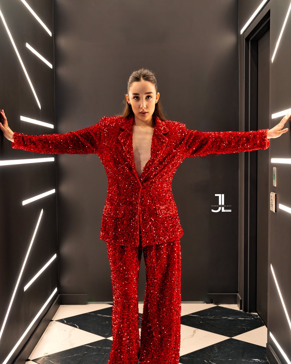 Woman in a red sequined suit with wide-leg trousers posing in a marble-floored hallway, editorial fashion portrait